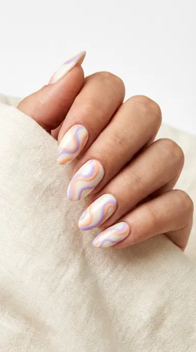 A close up editorial photograph of a woman's hand with medium length almond nails featuring hand painted swirl nail art