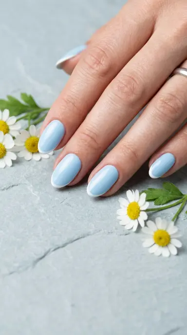A close up macro photograph of a woman's hand with short almond nails painted in a soft, opaque baby blue shade with a glossy finish