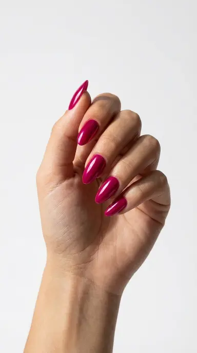 Bold editorial close-up of a woman's hand with almond nails in a saturated fuchsia pink