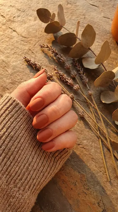 Close-up of a woman's hand with short oval nails in a warm terracotta clay shade