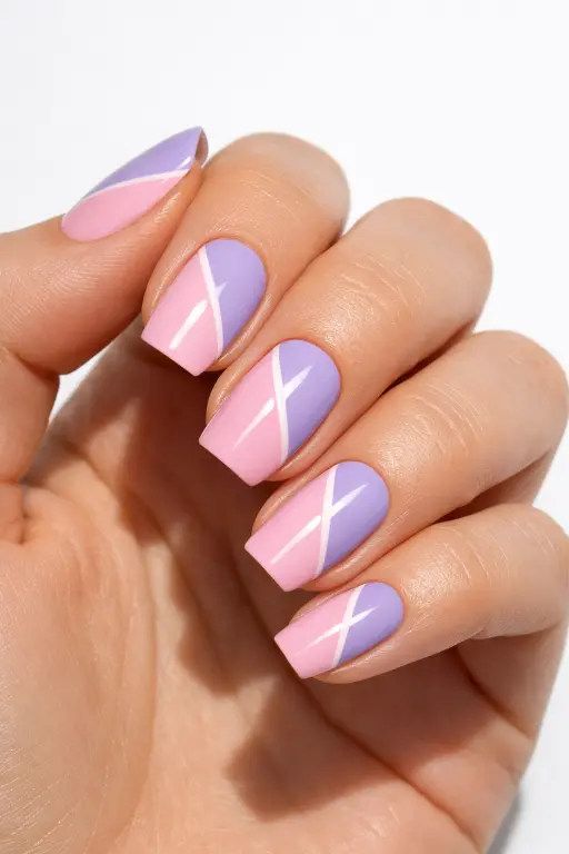 Close up photograph of a woman's hand with geometric nail art featuring diagonal color blocks of pastel pink and lavender