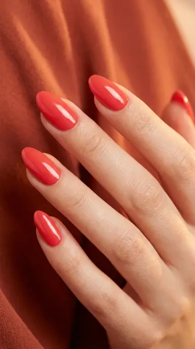 Editorial close-up of a woman's hand with almond-shaped nails in a vibrant coral red