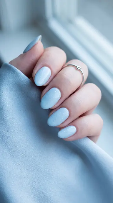 Macro photograph of short almond nails painted in a soft baby blue with a hint of fine shimmer